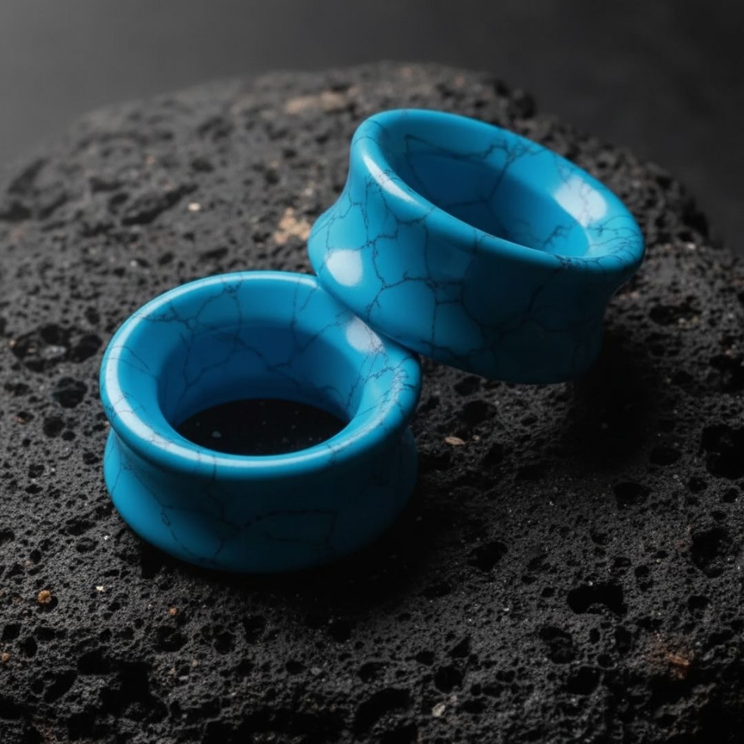 Pair of bright blue Turquoise stone tunnels (gauges) on a dark background. Organic double flare plugs for stretched ears.