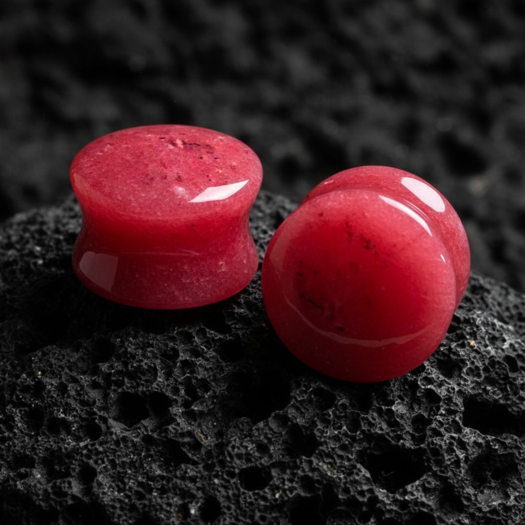 Close-up of a pair of polished, deep red jade stone ear plugs with a slight flare, showcasing their natural texture and color.