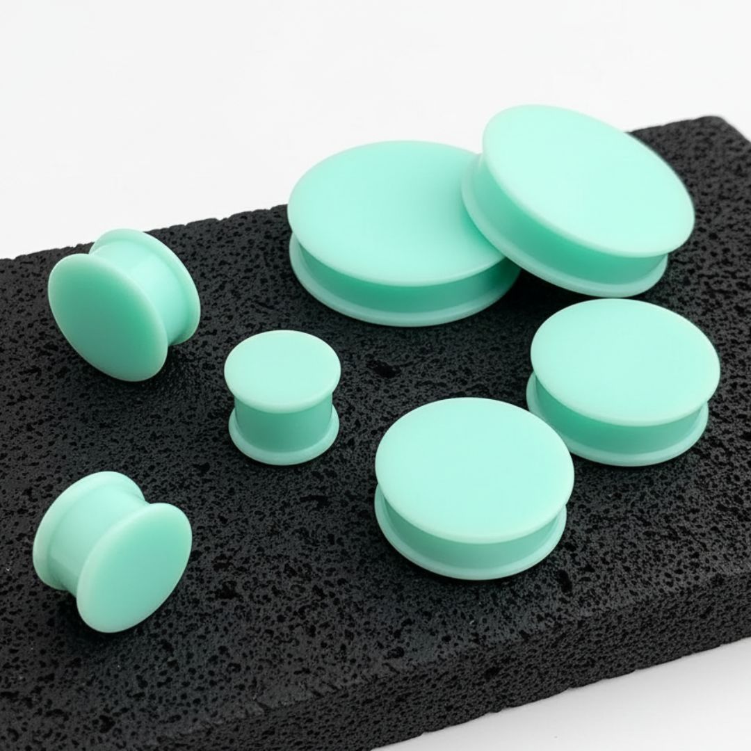 A pair of Teal Silicone Plugs (6mm-51mm) resting on stone against a white background.
