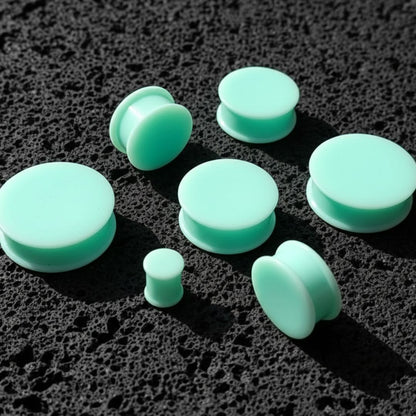Teal Silicone Plugs in various sizes (6mm-51mm) on dark volcanic rock with side light.