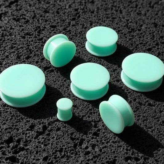 Teal Silicone Plugs in various sizes (6mm-51mm) on dark volcanic rock with side light.