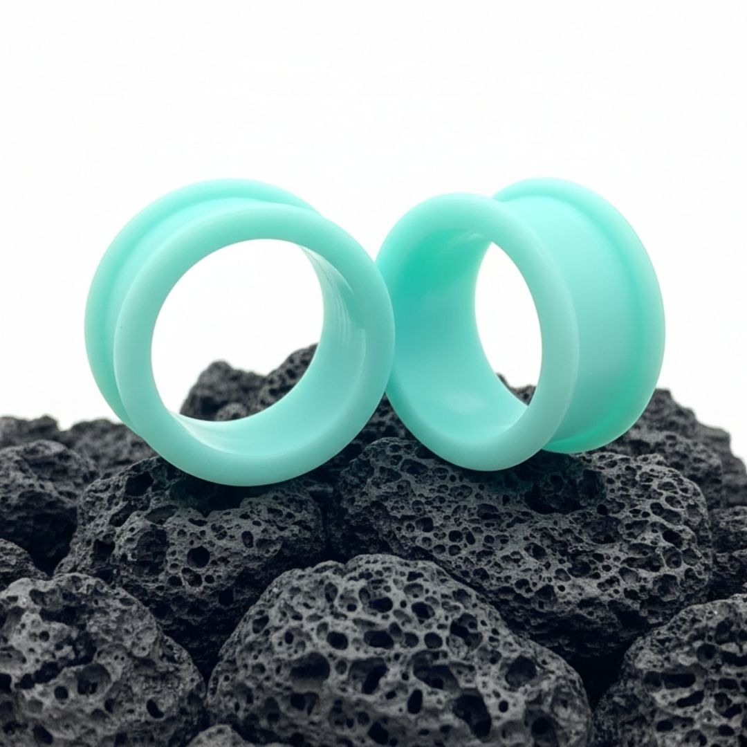 Pair of deep teal silicone tunnels (flexible gauges) displayed against a dark background, showing comfort for stretched ears.