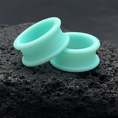 Pair of deep teal silicone tunnels (flexible gauges) displayed against a dark background, showing comfort for stretched ears.