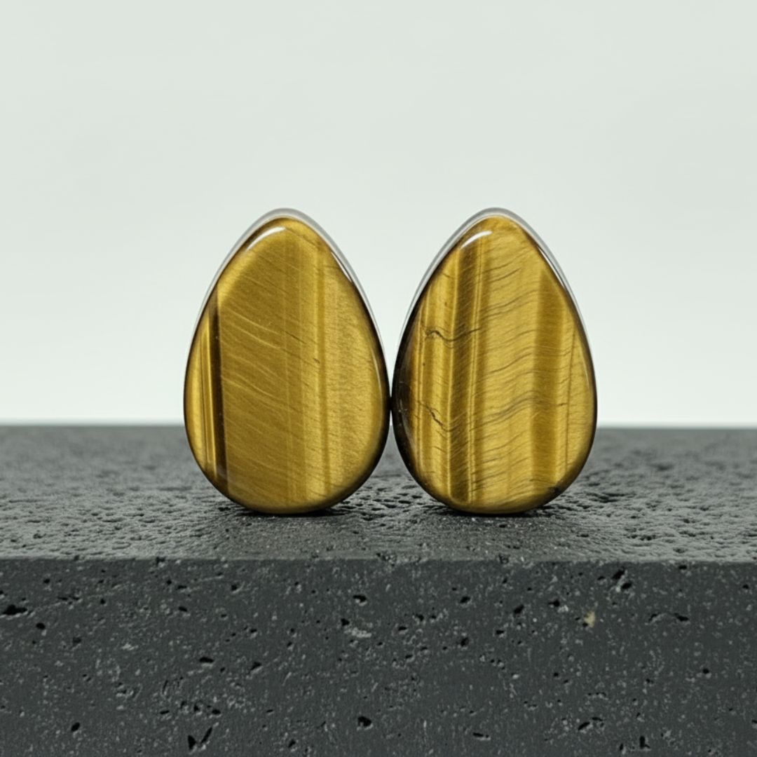 Tigers Eye Stone Teardrop Plugs (6mm-38mm) on a rock against a clean white studio background.