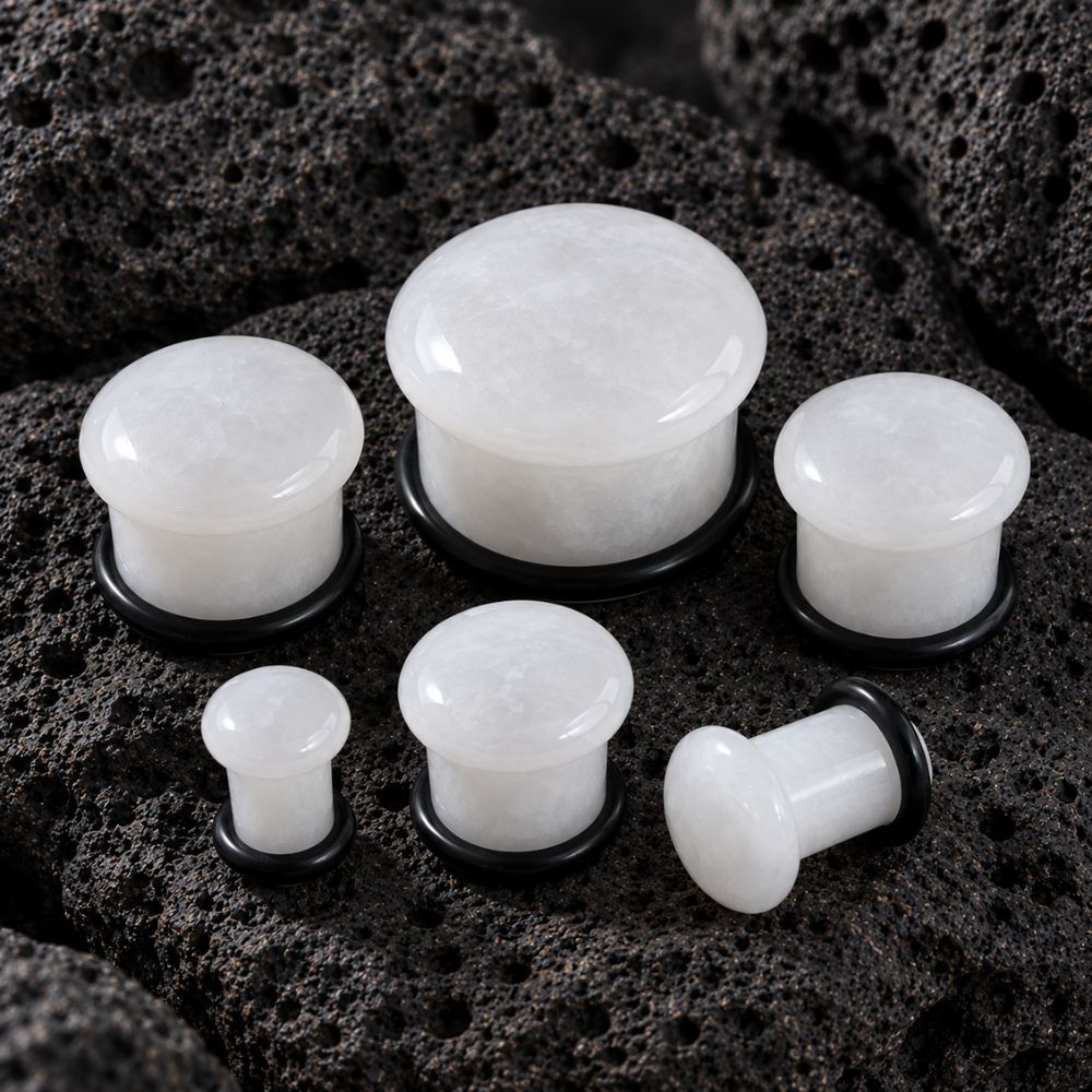 Whit Jade plug earrings with black backing rings, displayed on a dark porous rock background.
