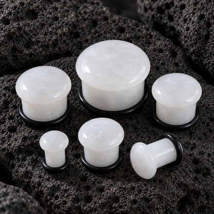 Whit Jade plug earrings with black backing rings, displayed on a dark porous rock background.