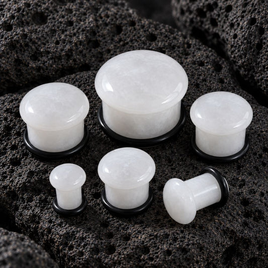 Whit Jade plug earrings with black backing rings, displayed on a dark porous rock background.