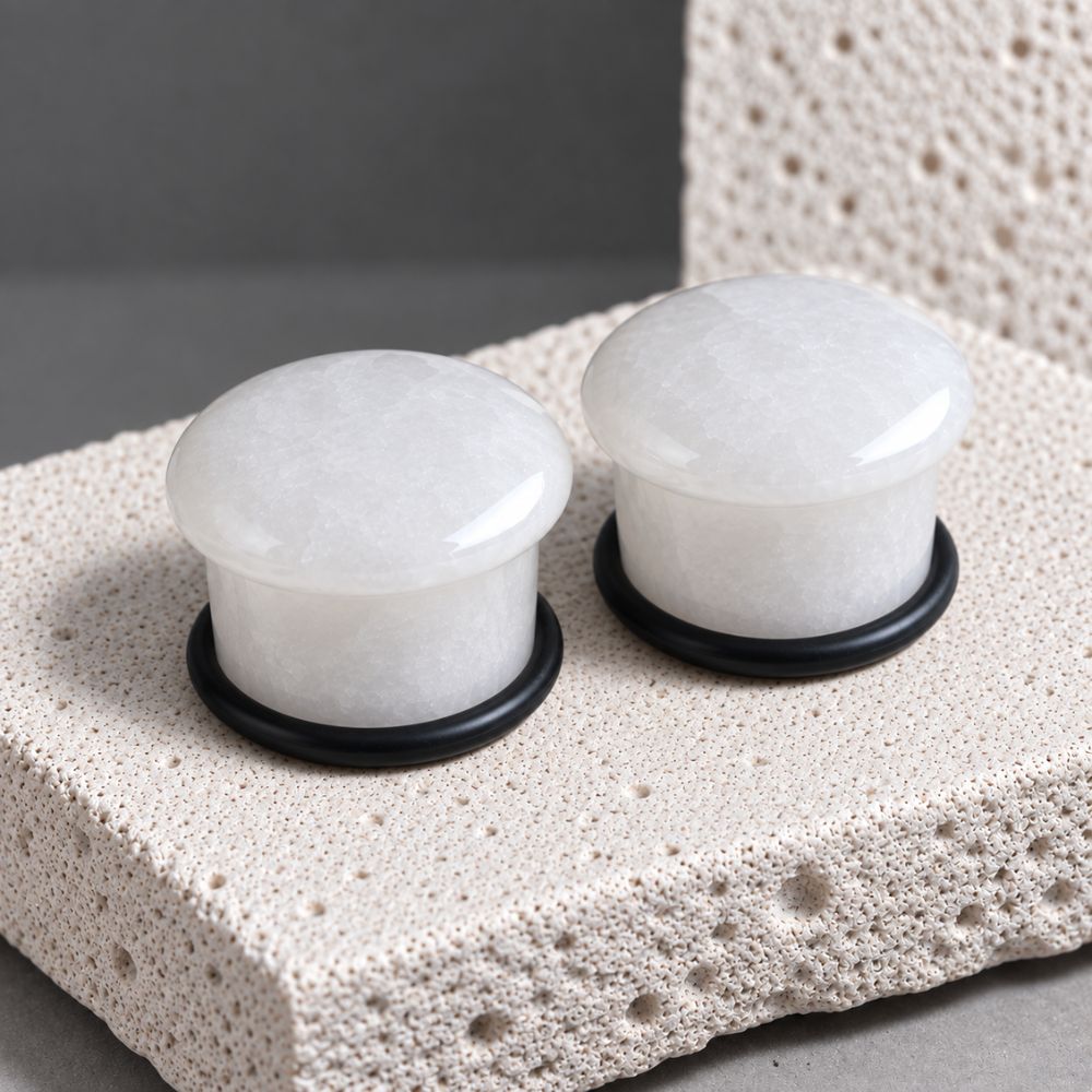 A pair of white jade stone gauges for stretched ears on a porous stone background