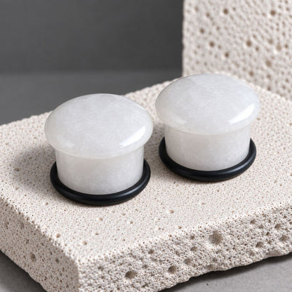 A pair of white jade stone gauges for stretched ears on a porous stone background