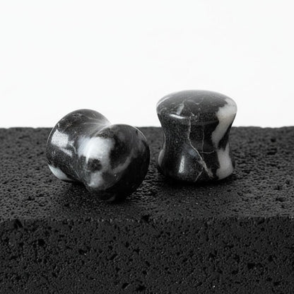 Two black and white marbled stones plugs on a textured black surface