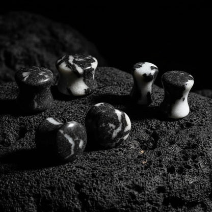 A pair of round Zebra Jasper stone plugs for stretched ears, displaying distinct black and white striped patterns on a white background.