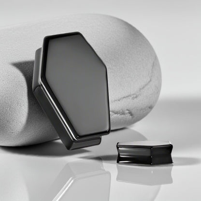air of obsidian coffin-shaped ear plugs with sleek black finish and sharp, angular design on a stone surface